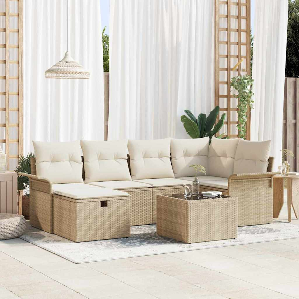 Outdoor-Sitzbereich mit beigen Korbmöbeln, weißen Kissen und einem Couchtisch mit Glasplatte. Weiße Vorhänge und Pflanzen im Hintergrund.