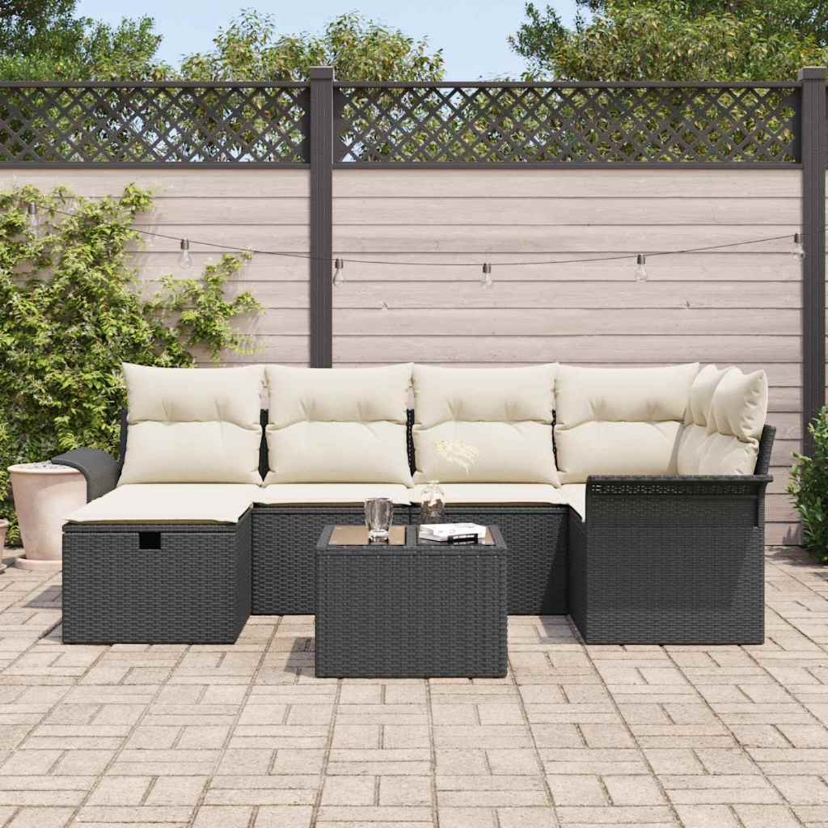 Garten-Terrassenset mit dunkelgrauen Möbeln, beigen Kissen und einem kleinen Tisch. Vor einem Holzzaun und Grün.