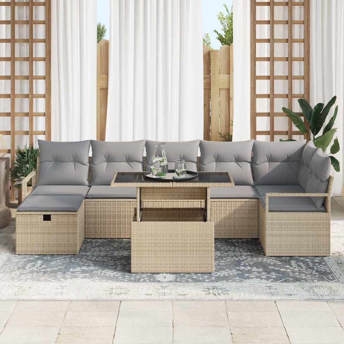 Sofá seccional exterior con cojines grises, una mesa y una alfombra. Cortinas y celosía de madera en el fondo. Jarra y vasos en la mesa.