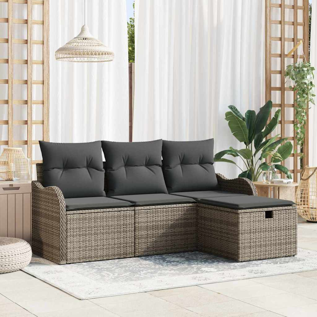 Rattansofa mit grauen Kissen, neben einer Pflanze und einem Fenster mit weißen Vorhängen. Eine Korblampe hängt.