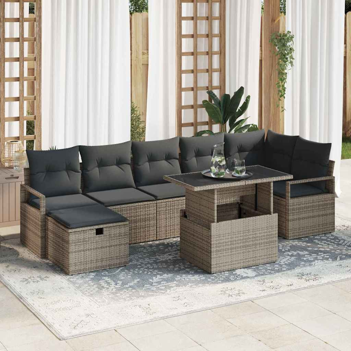Outdoor-Sitzbereich mit grauen Kissen, einem Couchtisch und einem Teppich. Weiße Vorhänge und Holzgitter im Hintergrund.