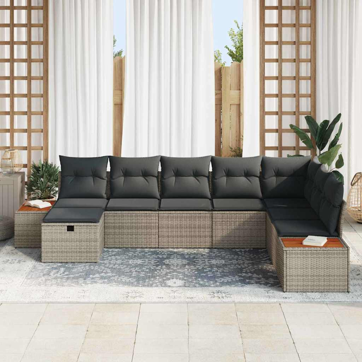 Sofá seccional exterior con cojines grises, base de mimbre y mesas de madera. Ventanas con cortinas blancas al fondo.