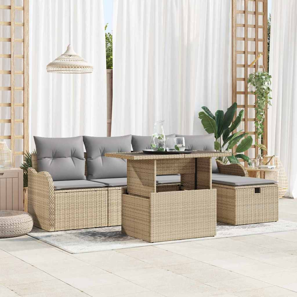 Outdoor-Sitzgruppe mit Möbeln im Korbstil, grauen Kissen und einem Tisch mit Hubplatte. Weiße Vorhänge und Pflanzen schaffen ein entspanntes Ambiente.