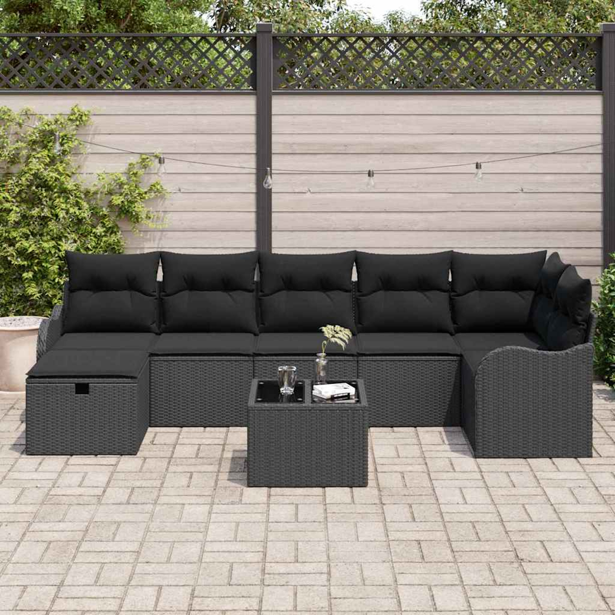 Schwarzes Outdoor-Geflecht-Ecksofa mit schwarzen Kissen und einem kleinen Tisch. Das Sofa steht auf einer Backstein-Terrasse mit Holzzaun im Hintergrund.