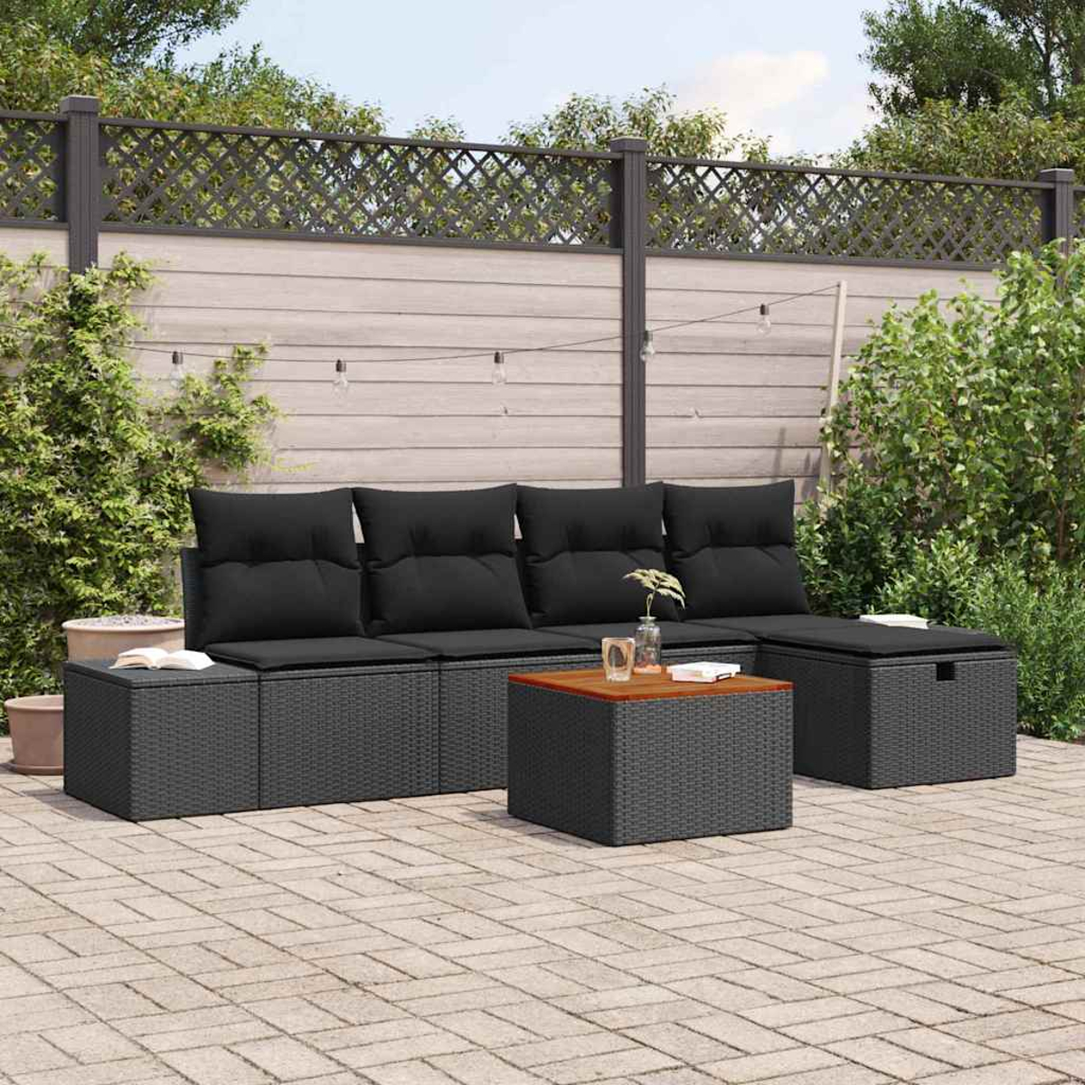 Garten-Terrassenset mit schwarzen Kissen und einem Holztisch. Der Hintergrund zeigt einen Holzzaun und üppiges Grün.