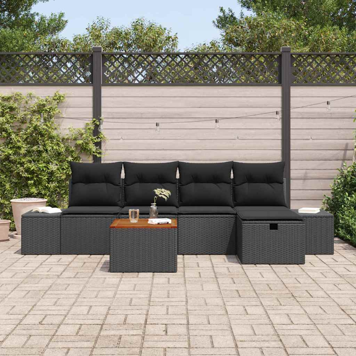 Gartenmöbel-Set mit schwarzen Kissen auf einer Ziegelterrasse vor einem Holzzaun.