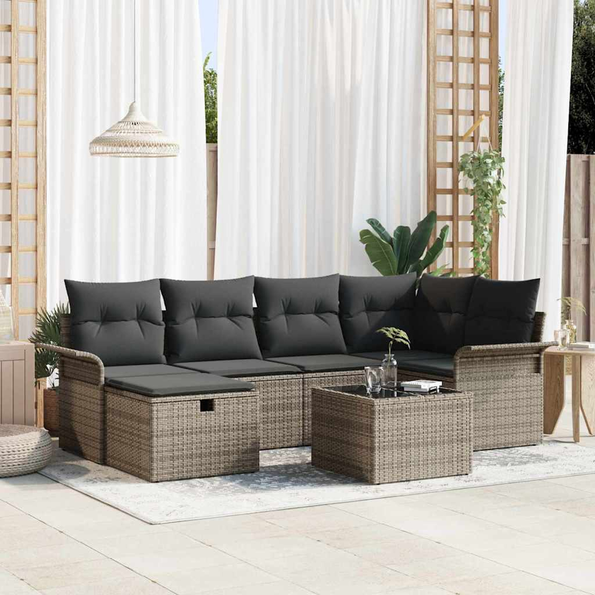 Garten-Sitzgruppe mit grauen Kissen und einem Couchtisch auf einer Terrasse. Weiße Vorhänge und hölzerner Spalier im Hintergrund.