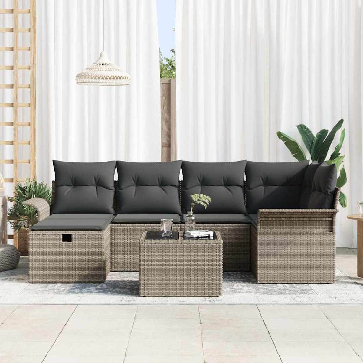 Outdoor-Rattan-Sofagarnitur mit dunklen Kissen. Davor ein kleiner Tisch und Getränke. Weiße Vorhänge im Hintergrund.