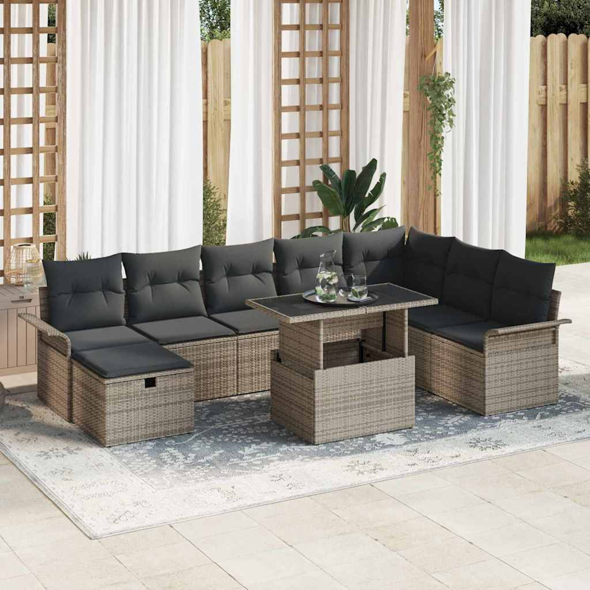 Terrassenset mit grauen Kissen, einem Tisch und einem Teppich. Weiße Vorhänge, Holzrahmen und Grünzeug im Hintergrund.