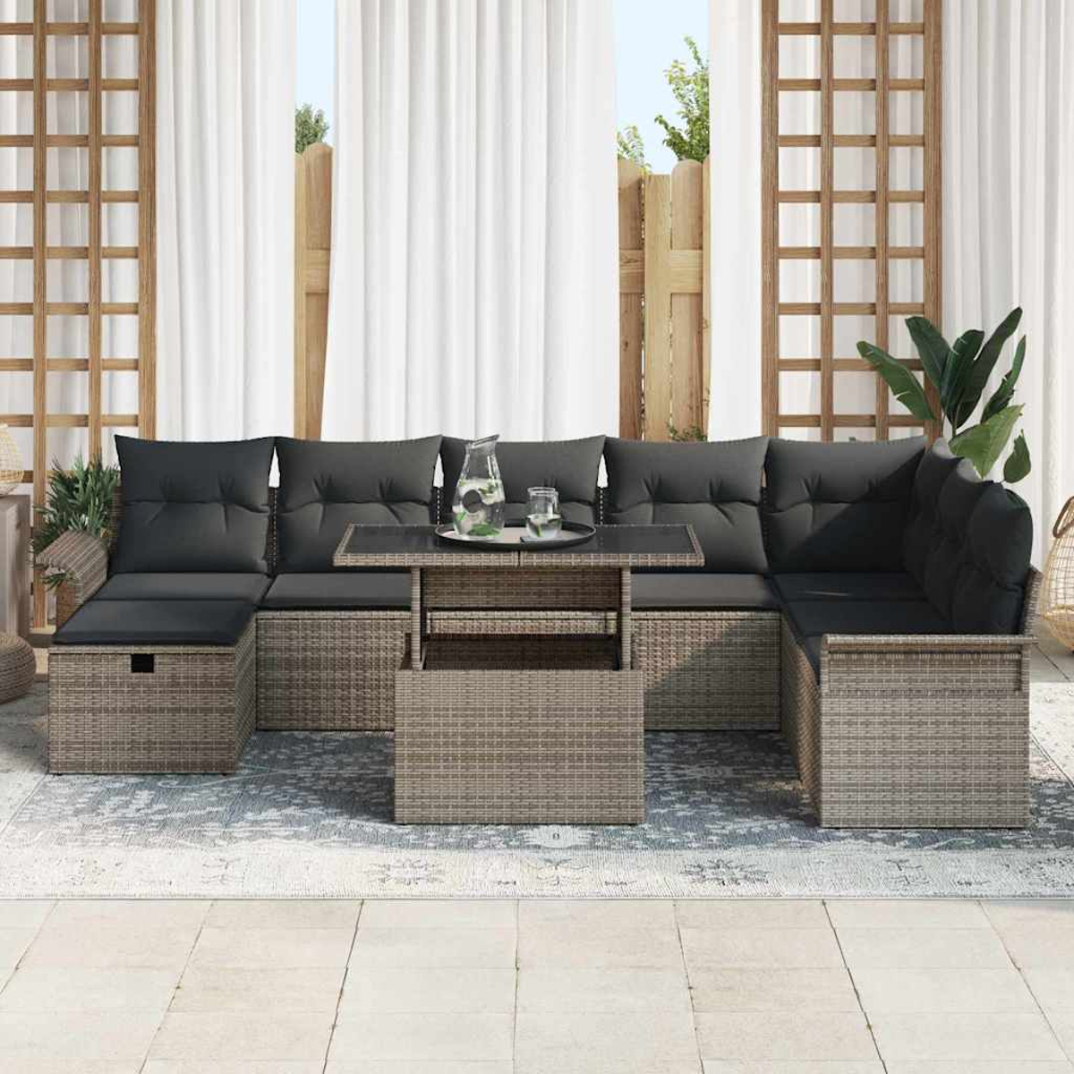 Gartensektionssofa mit schwarzen Kissen und einem Tisch mit Glasplatte, auf einem gemusterten Teppich. Weiße Vorhänge und Spalier im Hintergrund.
