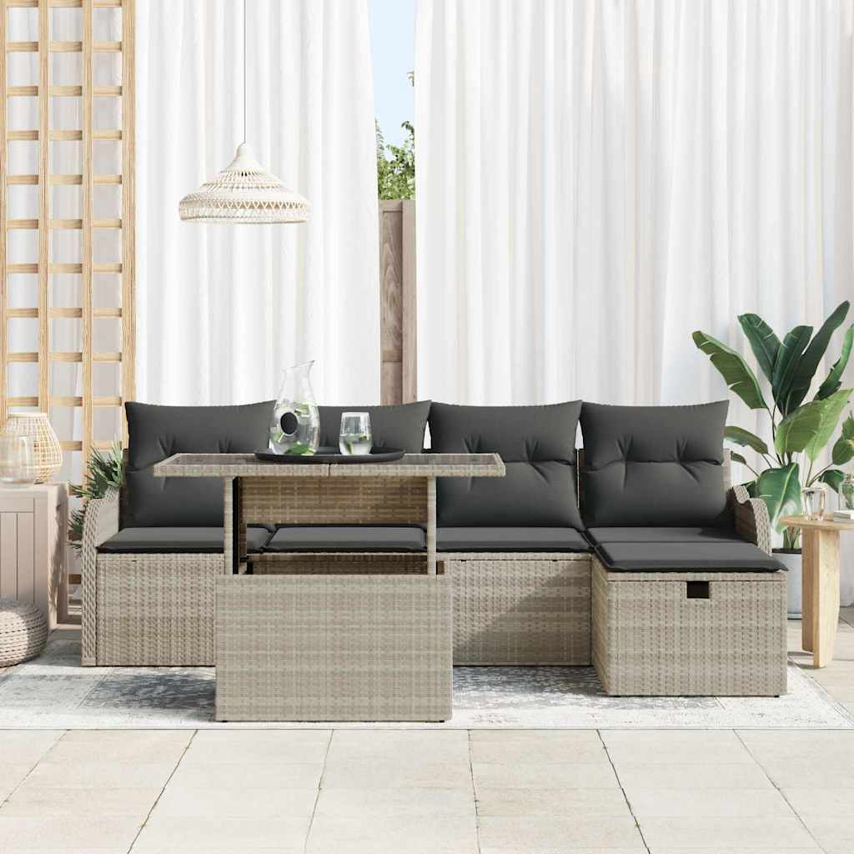 Outdoor-Sitzgruppe mit grauen Kissen und einem Tisch. Weiße Vorhänge im Hintergrund, rechts eine Pflanze.