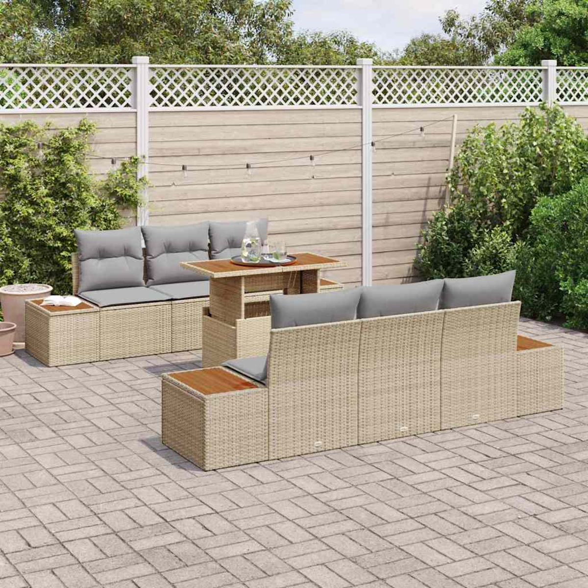 Gartenmöbel-Set aus Korbgeflecht auf einer Terrasse. Enthält Sofas, Tische und Kissen. Vor einem Zaun mit Pflanzen.
