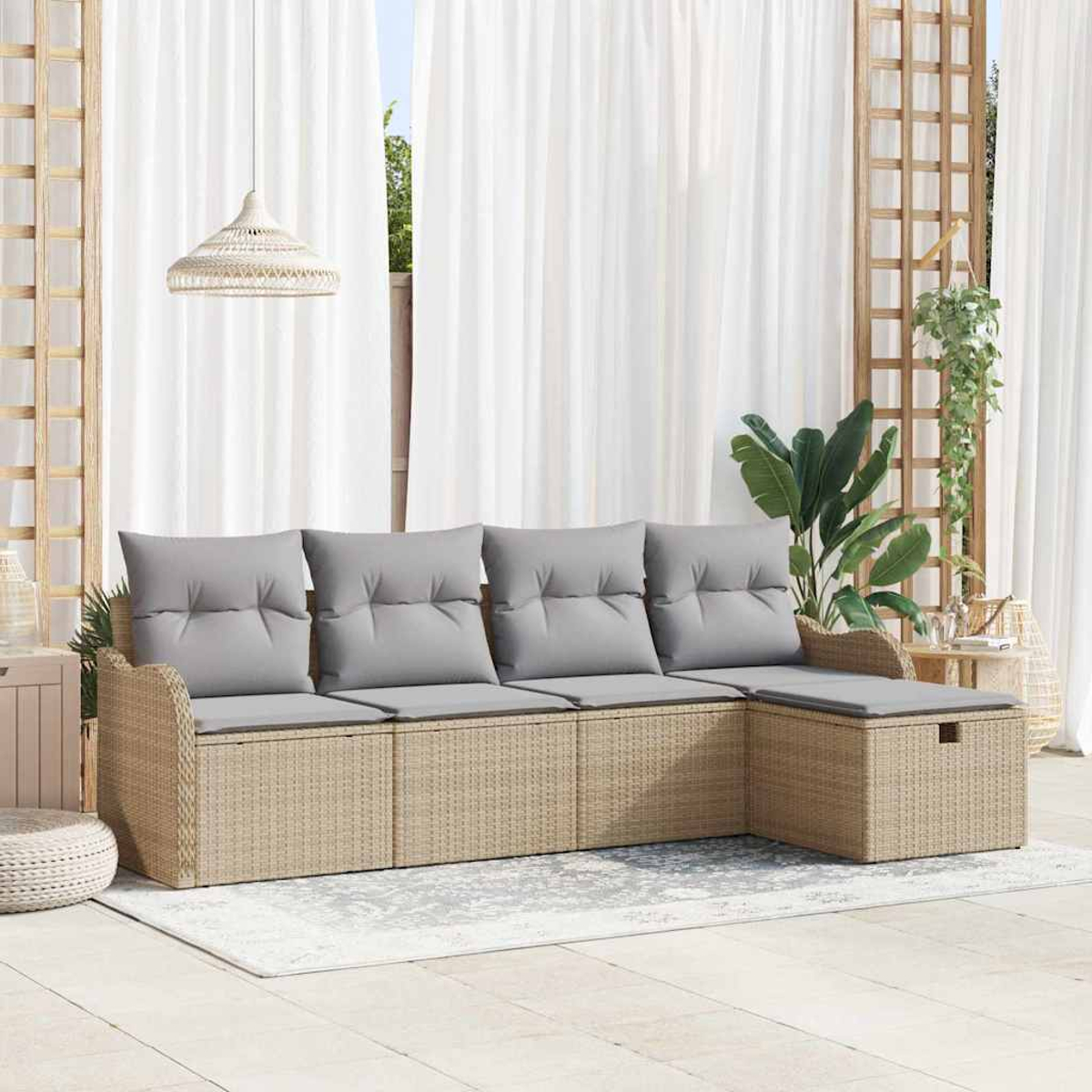 Ein Outdoor-Ecksofa aus Korbgeflecht mit grauen Kissen steht auf einem Teppich. Weiße Vorhänge und Pflanzen sind im Hintergrund.