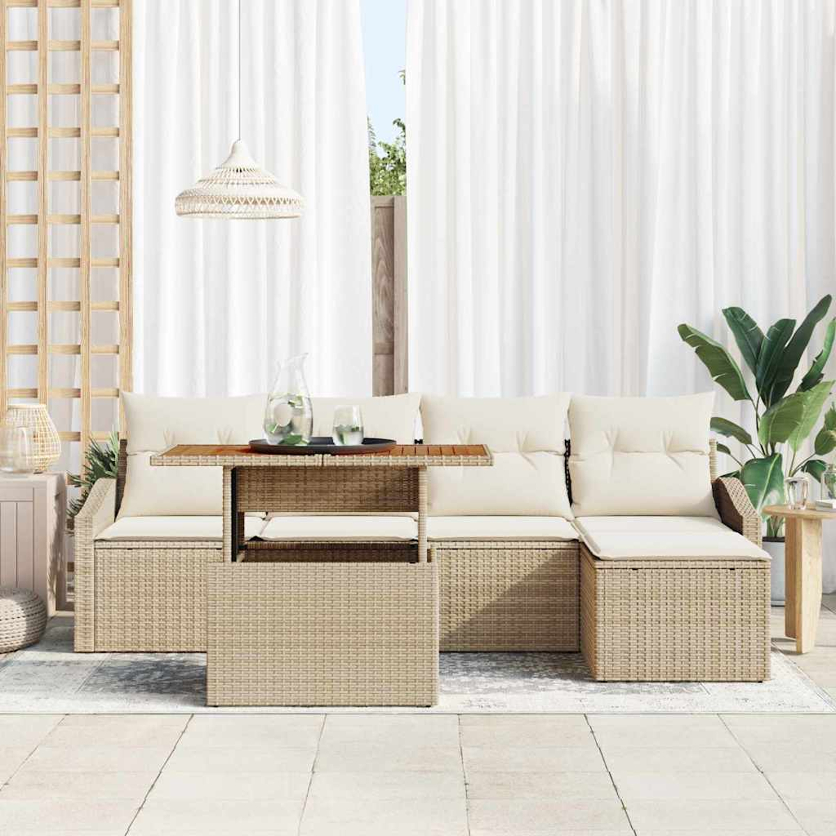 Outdoor-Sitzbereich mit beigen Korbmöbeln, cremefarbenen Kissen und einem Holztisch. Weiße Vorhänge und eine große Pflanze im Hintergrund.