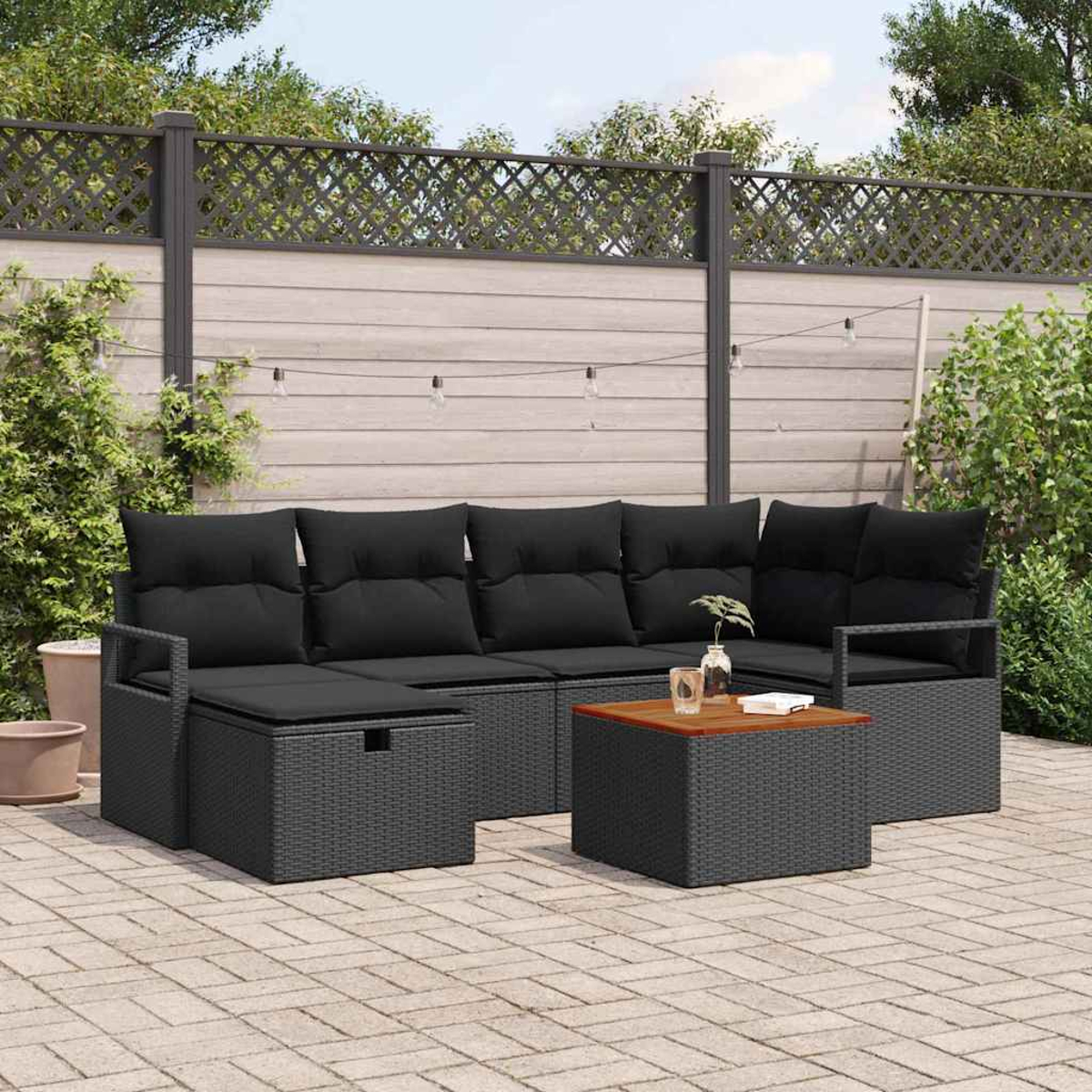 Gartenmöbel-Set, graues Rattan mit schwarzen Kissen. Enthält einen Couchtisch und steht auf einer Ziegelterrasse mit Zaun.