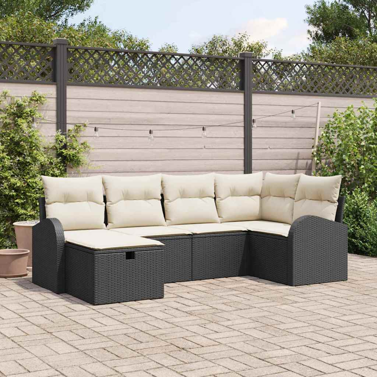 Outdoor-Ecksofa mit beigen Kissen. Dunkelgraue Korbstruktur. Vor einem Holzzaun und Grün.