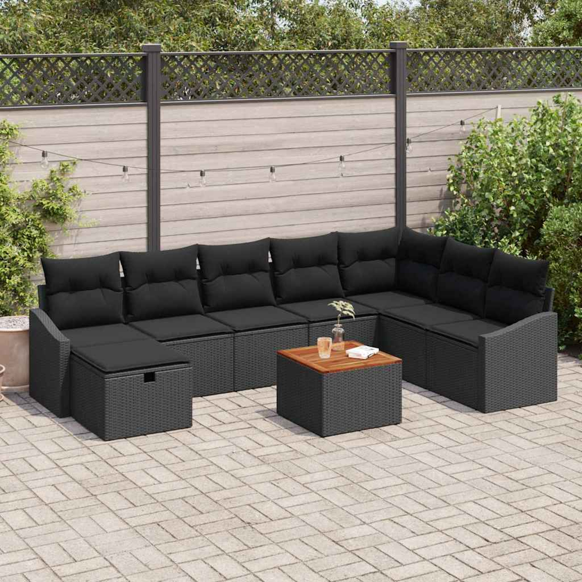 Outdoor-Ecksofa mit schwarzen Kissen. Ein Holztisch und eine graue Ziegelterrasse befinden sich davor. Im Hintergrund sind ein Zaun und Pflanzen.