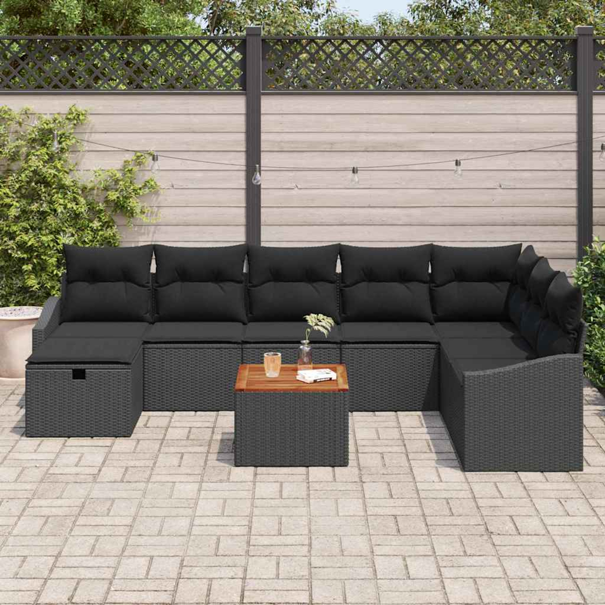 Outdoor-Ecksofa mit schwarzen Kissen und grauem Korbgewebe. Kleiner Holztisch mit Glas und Buch. Ziegelpflaster.