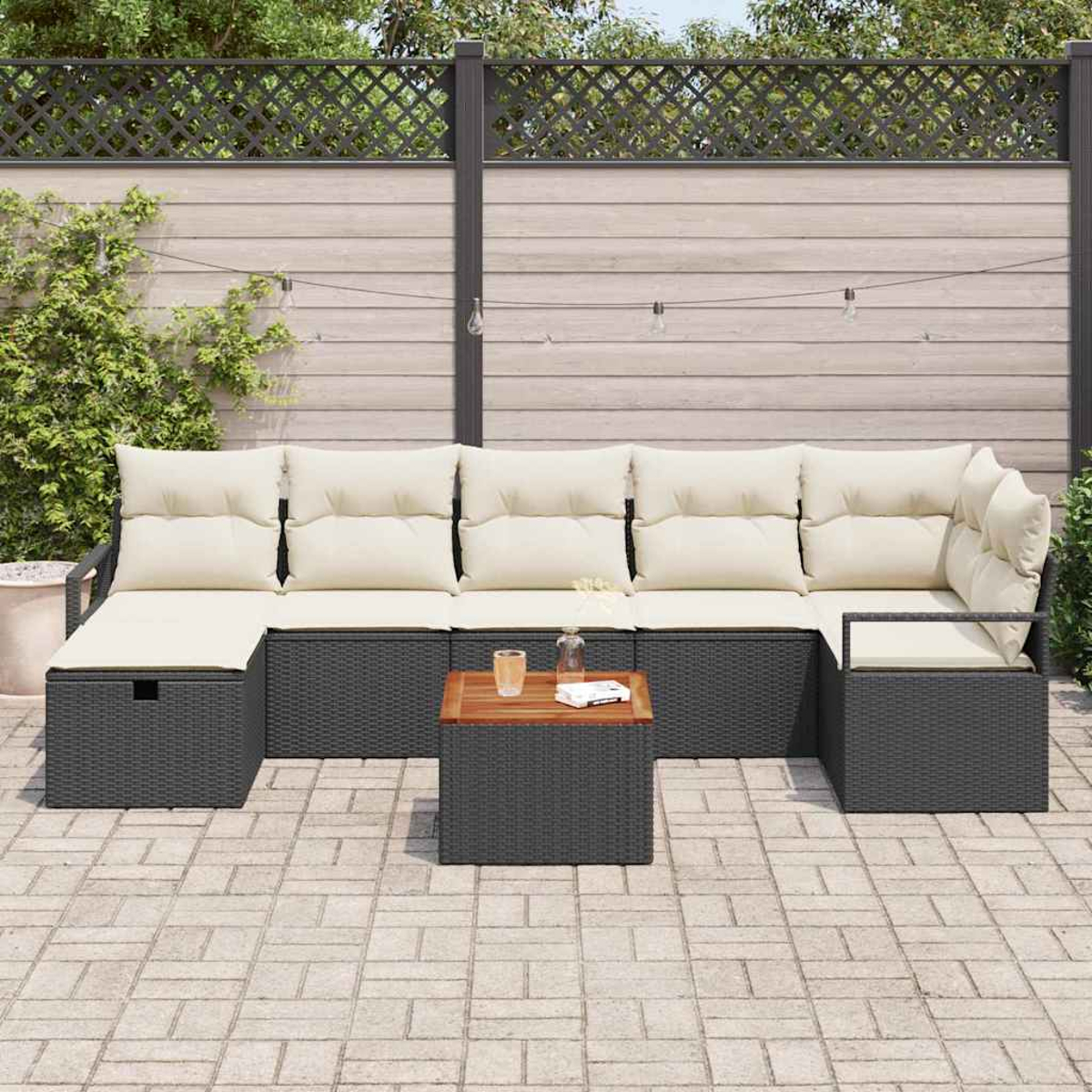 Schwarzes Outdoor-Korbmöbel mit beigen Kissen und einem Holztisch auf einer Terrasse. Im Hintergrund befinden sich ein Zaun und Pflanzen.