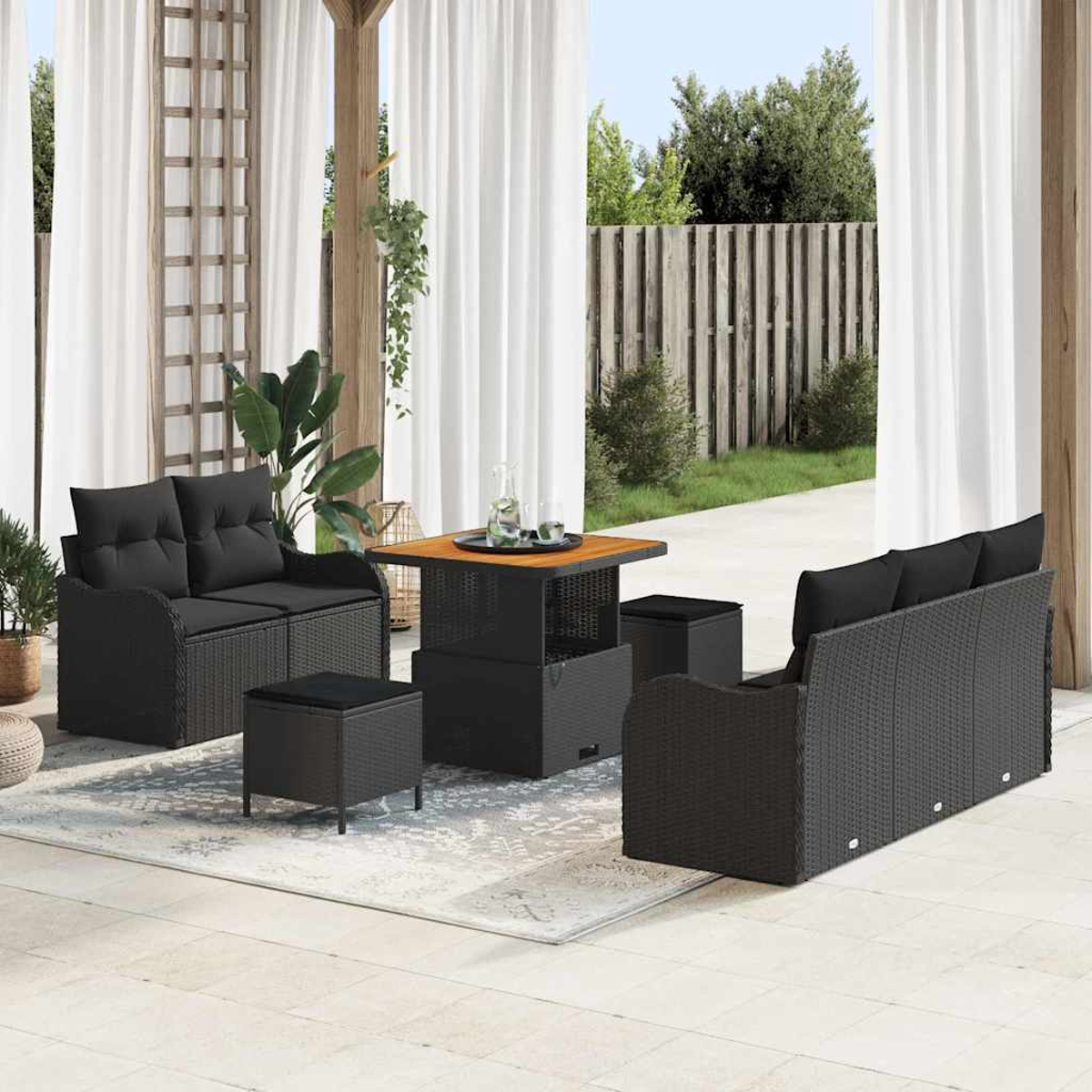 Terrassenset im Freien mit schwarzen Korbmöbeln: Sofa, Liebesitz, Ottomanen und ein Tisch. Weiße Vorhänge und ein Holzzaun sind im Hintergrund.