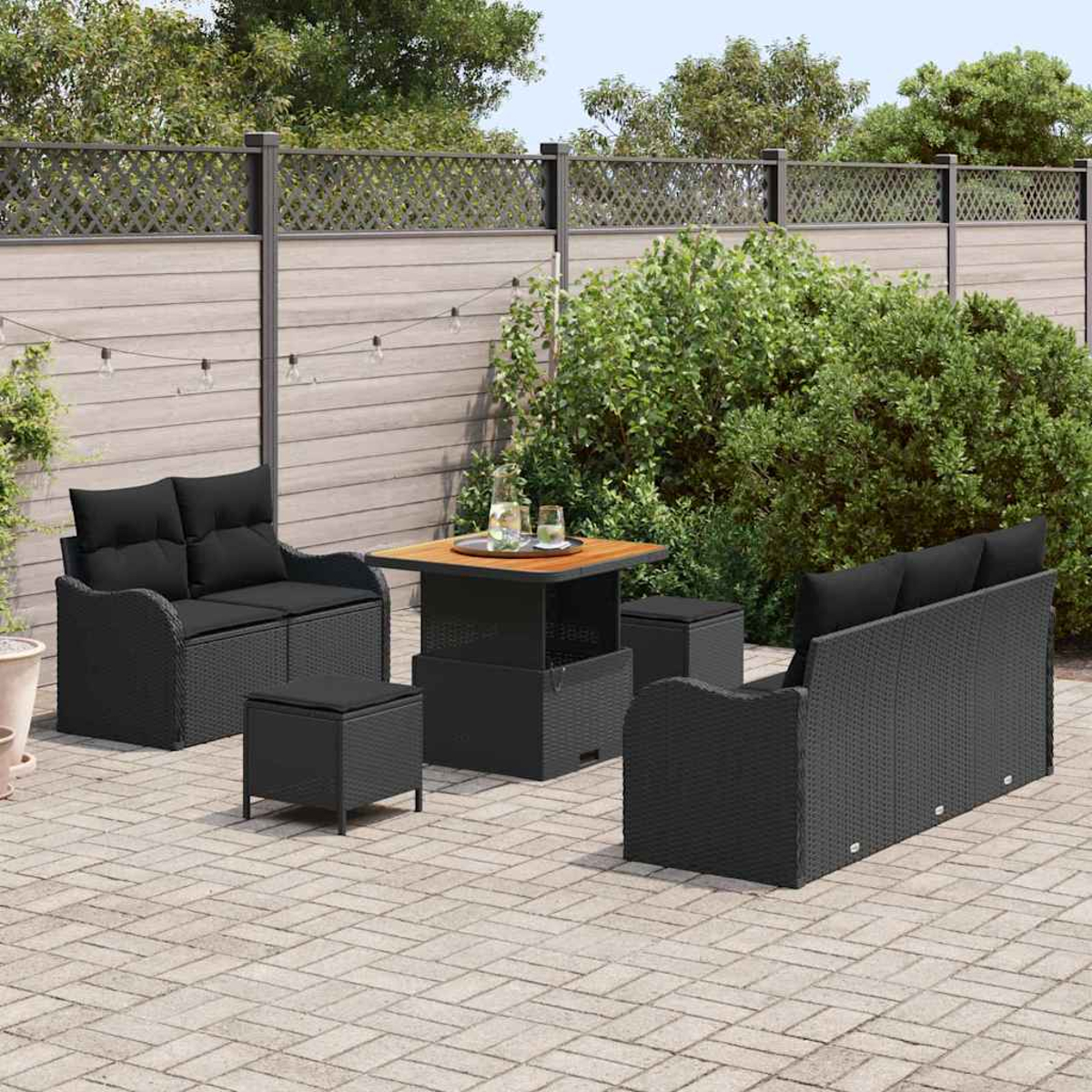 Terrassenset mit schwarzem Korbmöbeln, bestehend aus Sofa, Zweisitzer, Ottomanen und einem Tisch mit Holzplatte, auf einer Terrasse.
