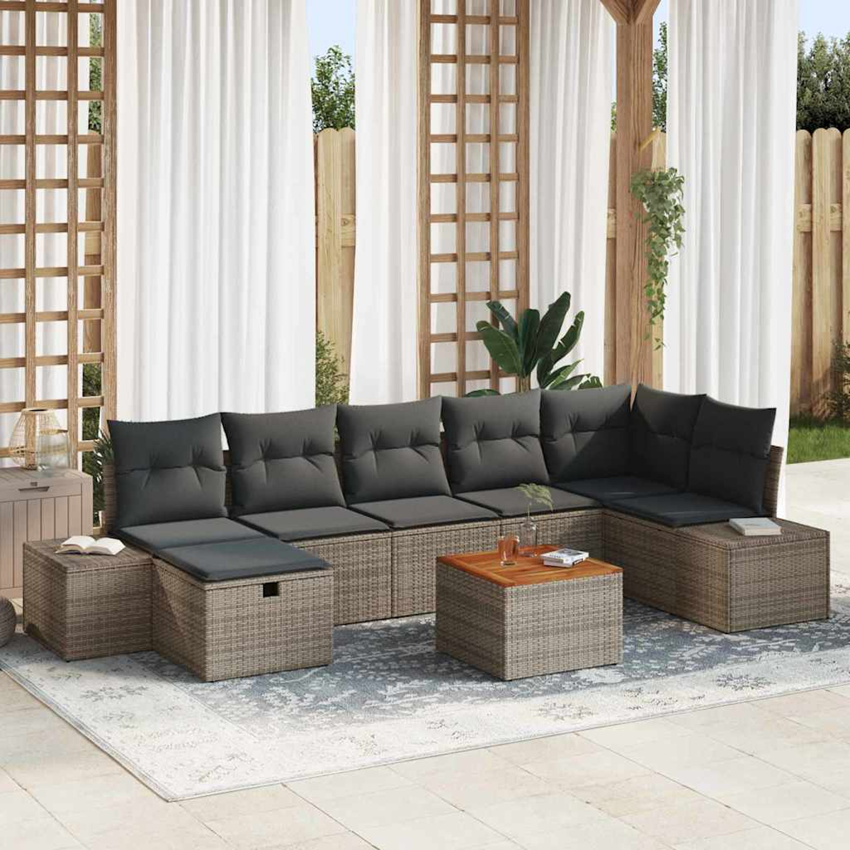 Outdoor-Ecksofa mit grauen Kissen, zwei Ottomanen und einem kleinen Holztisch auf einem gemusterten Teppich. Weiße Vorhänge und Holzgitter.