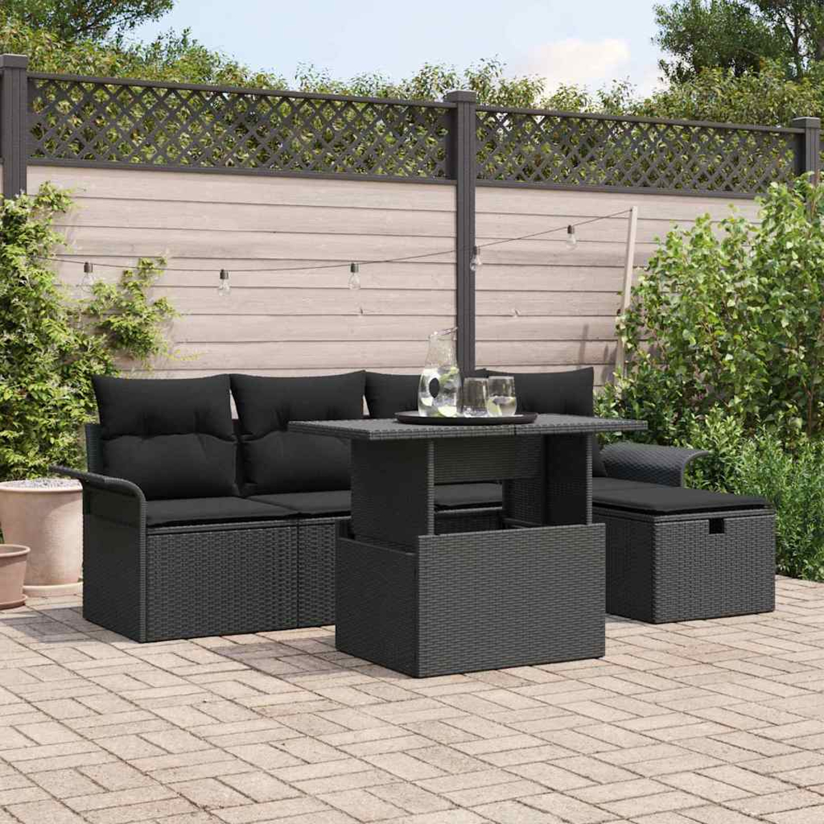 Ein schwarzes Terrassenset mit Sofa, Tisch und Stauraum. Ein Glaskrug und Gläser auf dem Tisch. Ein Holzzaun im Hintergrund.