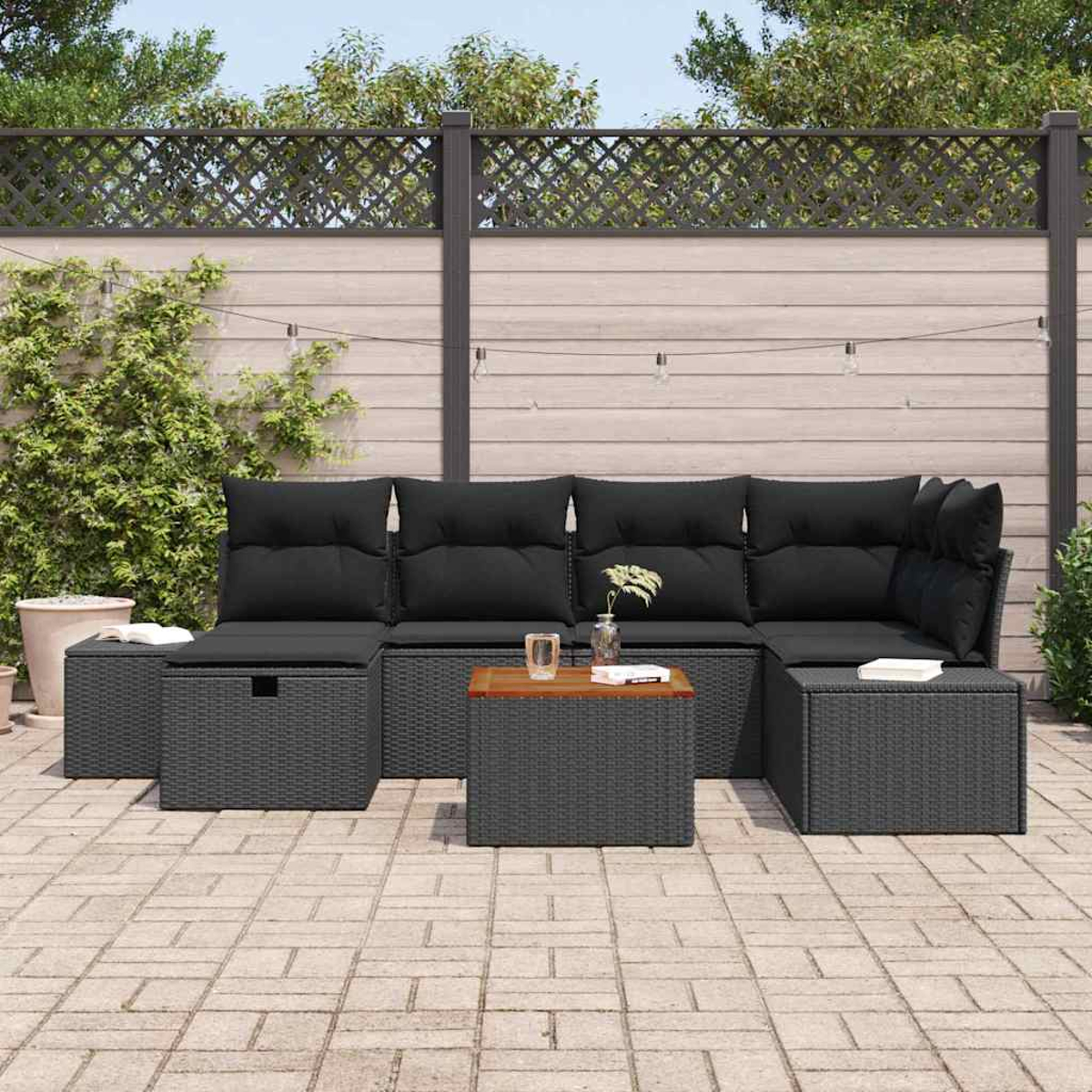 Ein Ecksofa im Freien mit schwarzen Kissen. Ein Holztisch und zwei Ottomanen stehen davor. Im Hintergrund ist eine Wand.