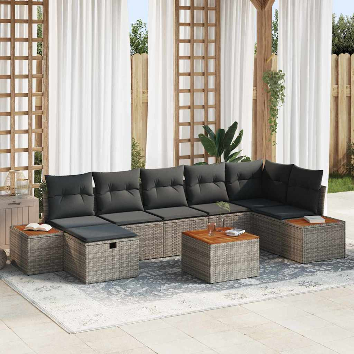 Graues Outdoor-Ecksofa aus Korbgeflecht mit dunkelgrauen Kissen und kleinen Holztischen. Weiße Vorhänge und ein gemusterter Teppich sind sichtbar.