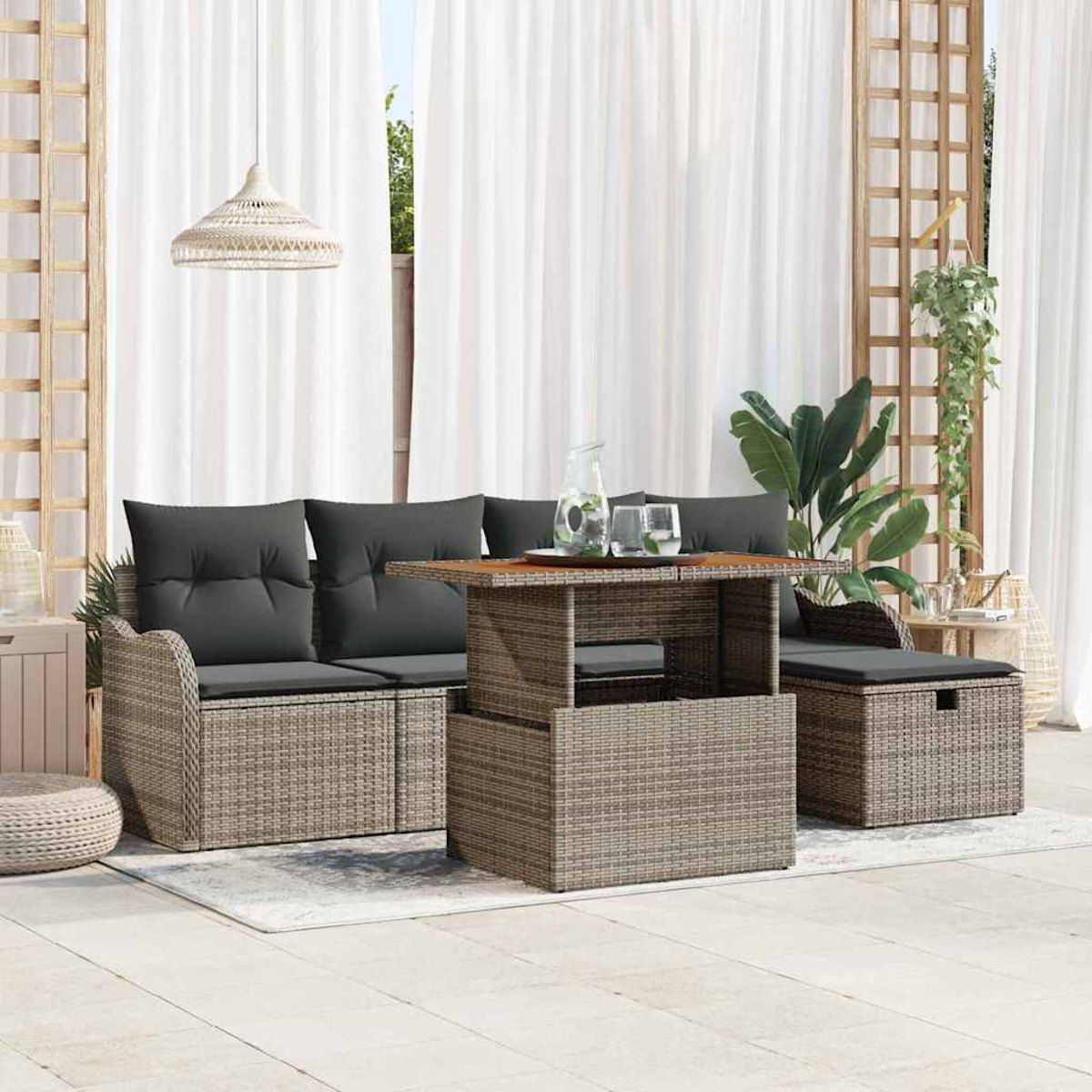Gartensitzgruppe mit Tisch, Sofa und Ottoman. Graue Kissen auf Korbmöbeln, weiße Vorhänge im Hintergrund und Pflanzen.