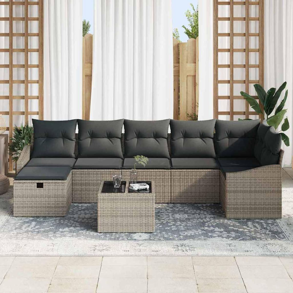 Graues Outdoor-Ecksofa aus Korbgeflecht mit Kissen, einem kleinen Tisch und einem Teppich. Weiße Vorhänge und Holzgitter im Hintergrund.