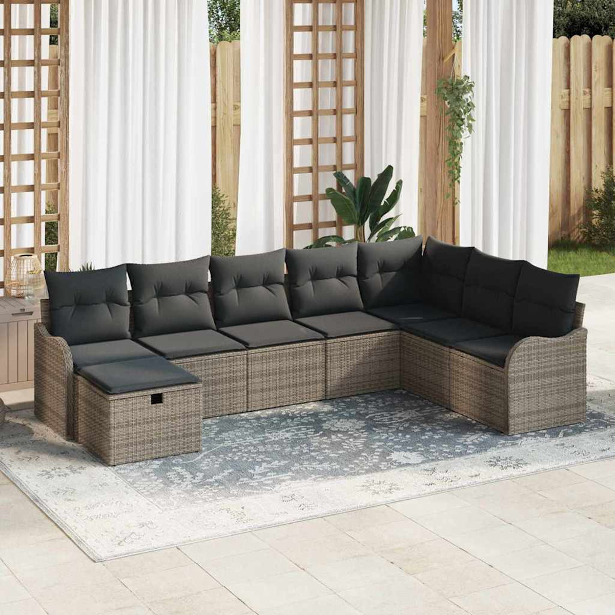 Ein Ecksofa im Freien mit grauen Kissen steht auf einem gemusterten Teppich. Weiße Vorhänge und Holzkonstruktionen sind im Hintergrund.