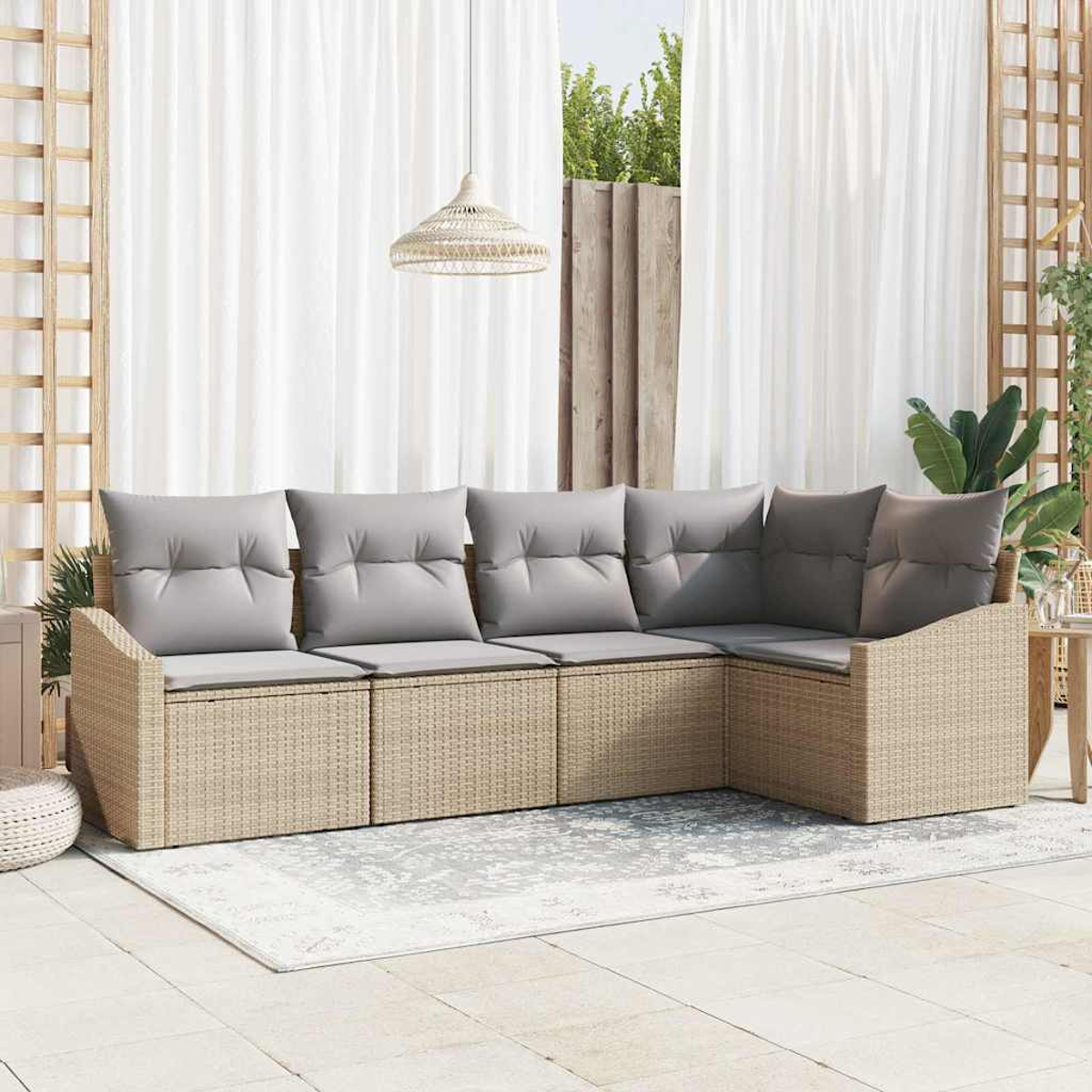 Ein Ecksofa aus Rattan mit grauen Kissen im Freien, auf einem gemusterten Teppich. Weiße Vorhänge und eine Hängelampe im Hintergrund.