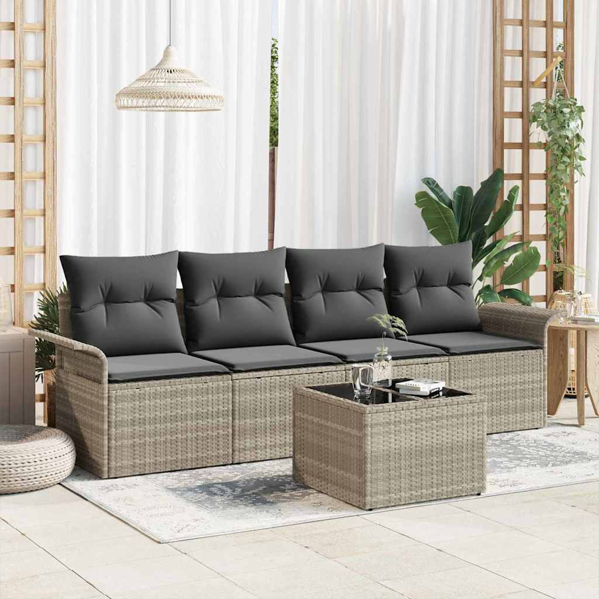 Szene im Freien mit einem Rattansofa und einem Couchtisch. Graue Kissen, weiße Vorhänge, Hängepflanzen und eine gewebte Lampe sind sichtbar.