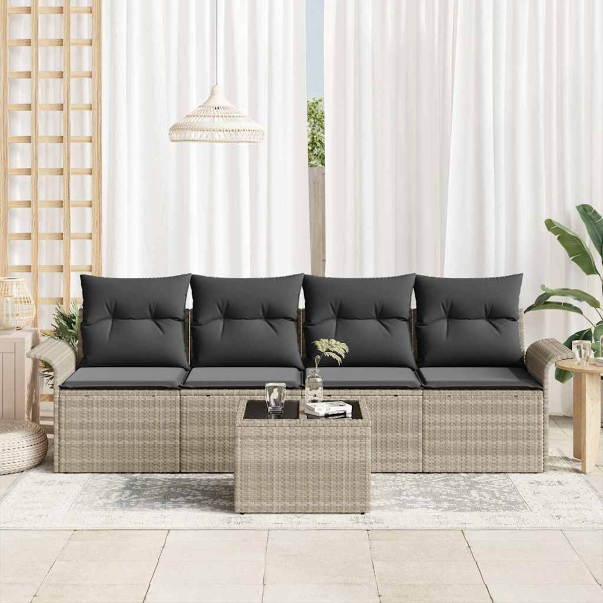 Ein Rattansofa mit grauen Kissen und einem passenden Tisch, vor weißen Vorhängen. Darüber hängt eine Hängelampe.