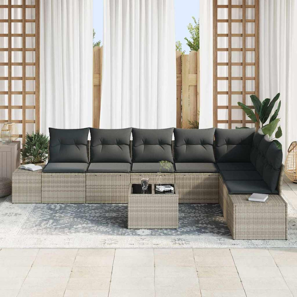 Outdoor-Ecksofa mit grauen Kissen, kleiner Tisch mit Glas und Buch. Weiße Vorhänge und Holzgitter im Hintergrund.