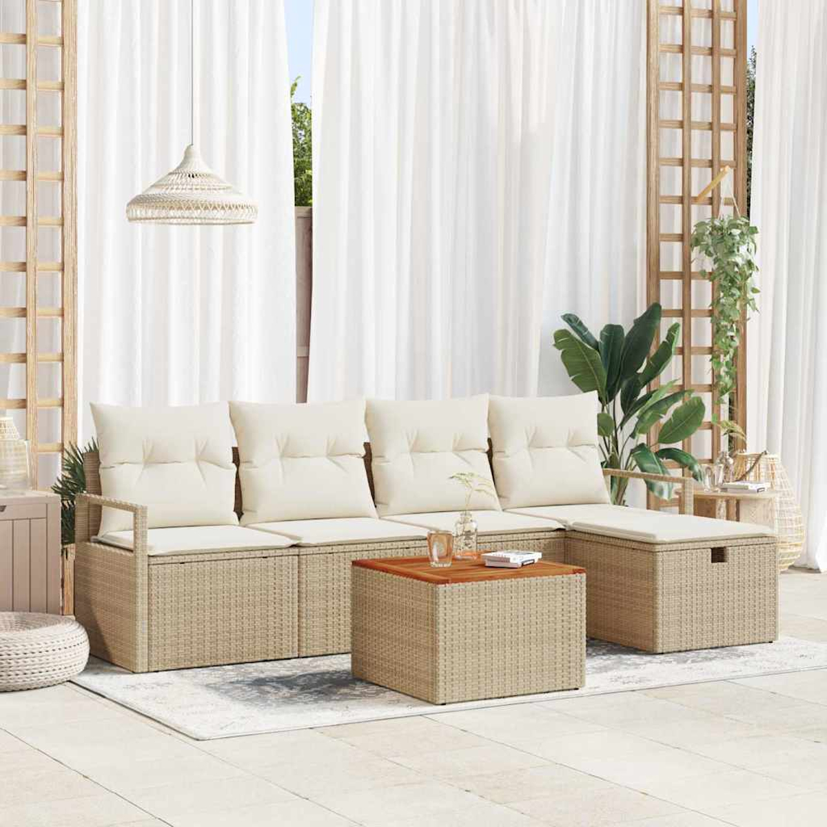 Zona de asientos al aire libre con cojines beige, una mesa de madera y una estructura tejida. Cortinas blancas al fondo. Hay plantas y decoración.