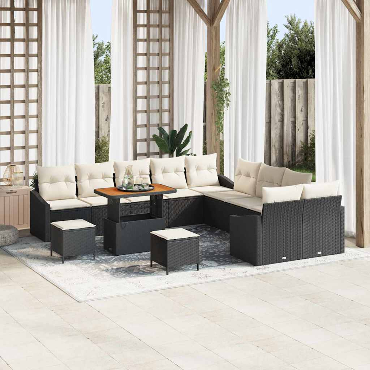 Gartenmöbel-Set. Schwarzes Rattan-Sofa mit cremefarbenen Kissen, Couchtisch und Ottomanen auf einem Teppich unter einem Baldachin und Vorhängen.