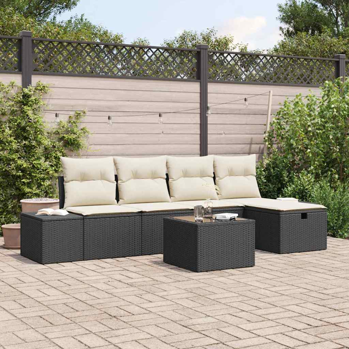 Gartenmöbel-Set: schwarzes Korbmöbel mit cremefarbenen Kissen, Couchtisch und Stauraumhocker auf einer Ziegelterrasse.