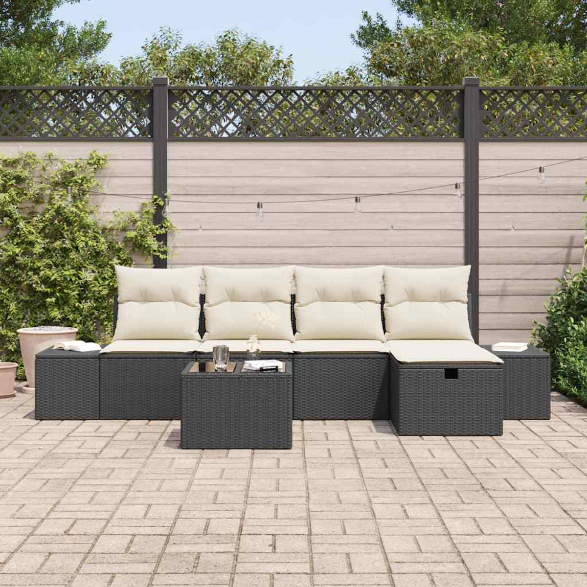 Outdoor-Terrassenset mit grau gewebten Möbeln und cremefarbenen Kissen. Enthält Sofa, Ottomanen und einen Couchtisch. Vor einem Zaun und Grün.