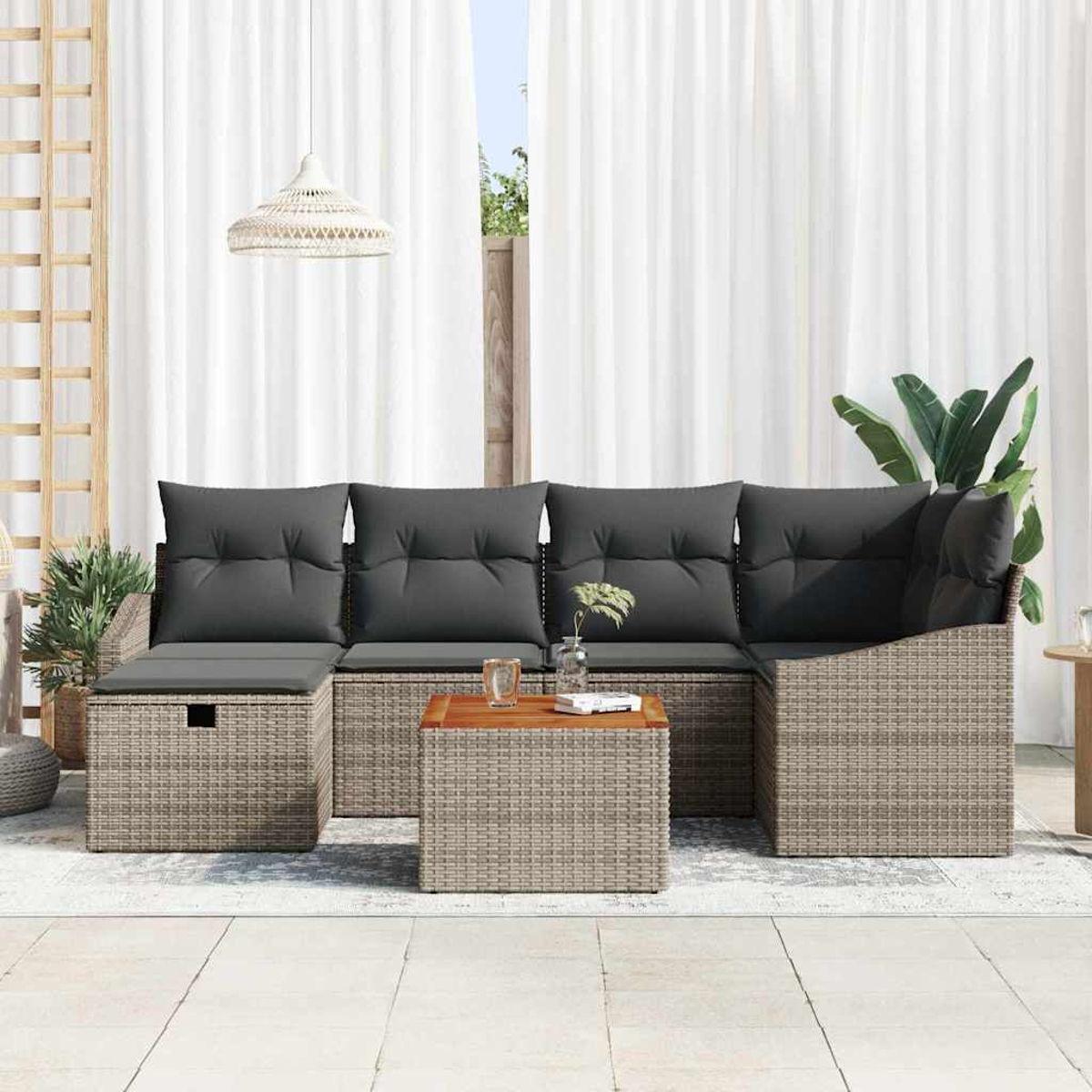 Rattansofa im Freien mit grauen Kissen und Holztisch. Weiße Vorhänge im Hintergrund. Pflanzen an den Seiten.
