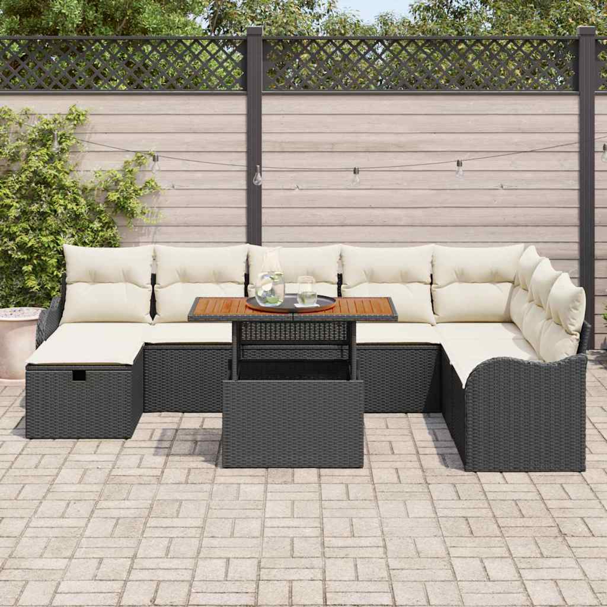 Outdoor-Ecksofa mit cremefarbenen Kissen und einem Holztisch. Graue Korbmöbel auf einer Terrasse mit Holzzaun.