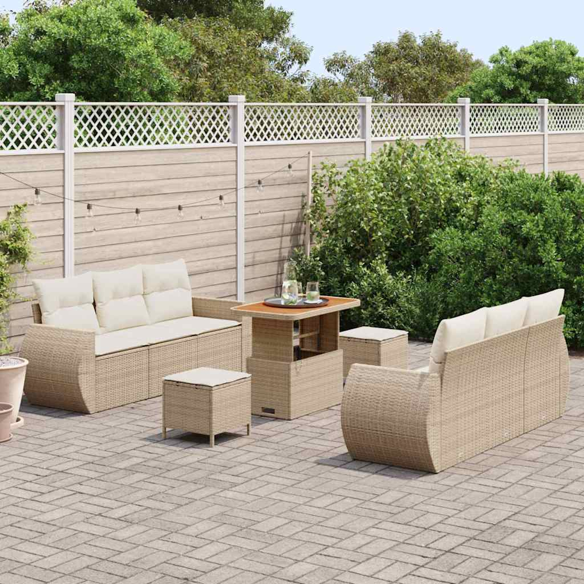 Juego de patio al aire libre con muebles de mimbre beige, cojines y una mesa de centro, colocados en un patio de ladrillos, con una valla y plantas al fondo.