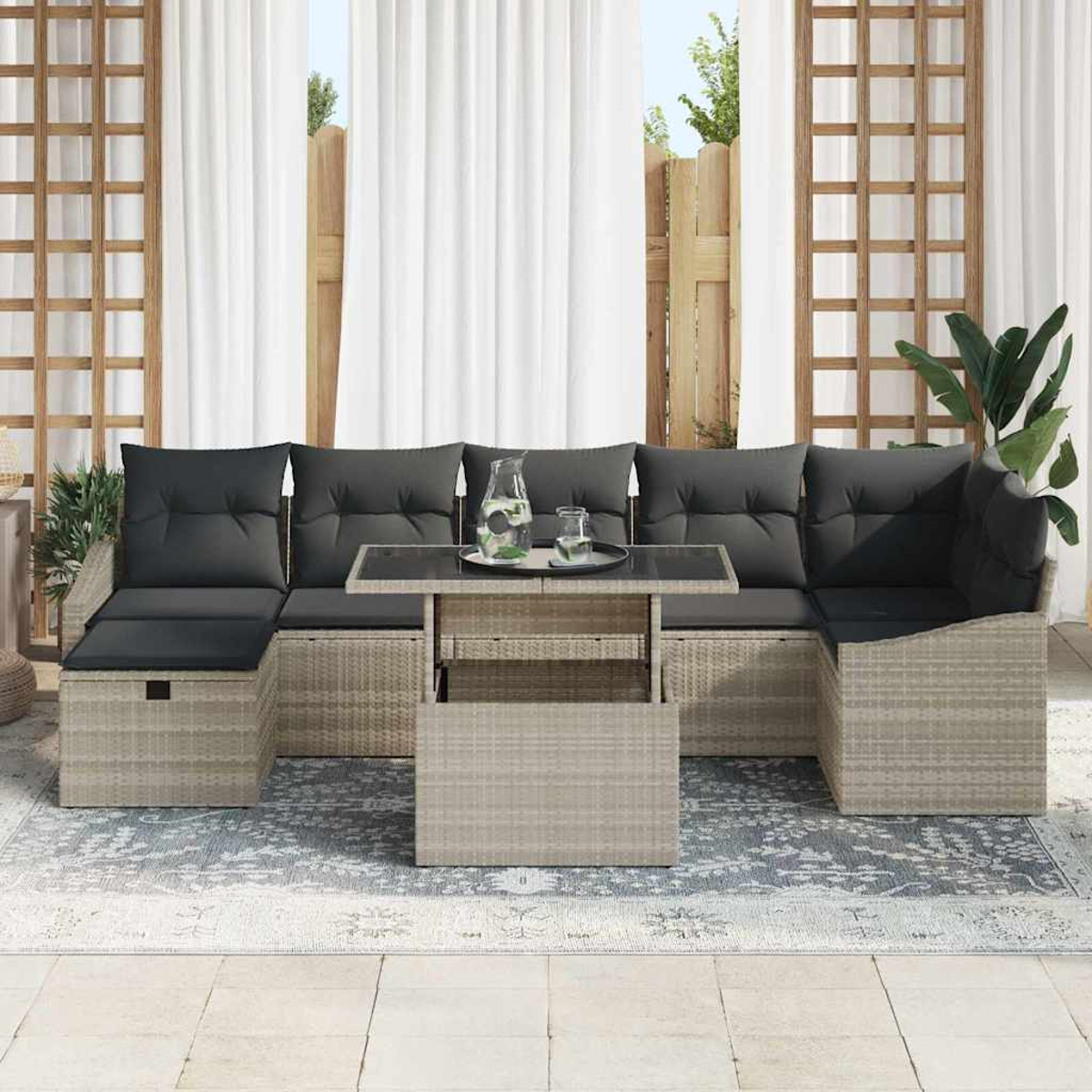 Gartenmöbel mit grauen Kissen, Tisch und Teppich. Weiße Vorhänge und Holzgitter im Hintergrund. Ein Glas Wasser.