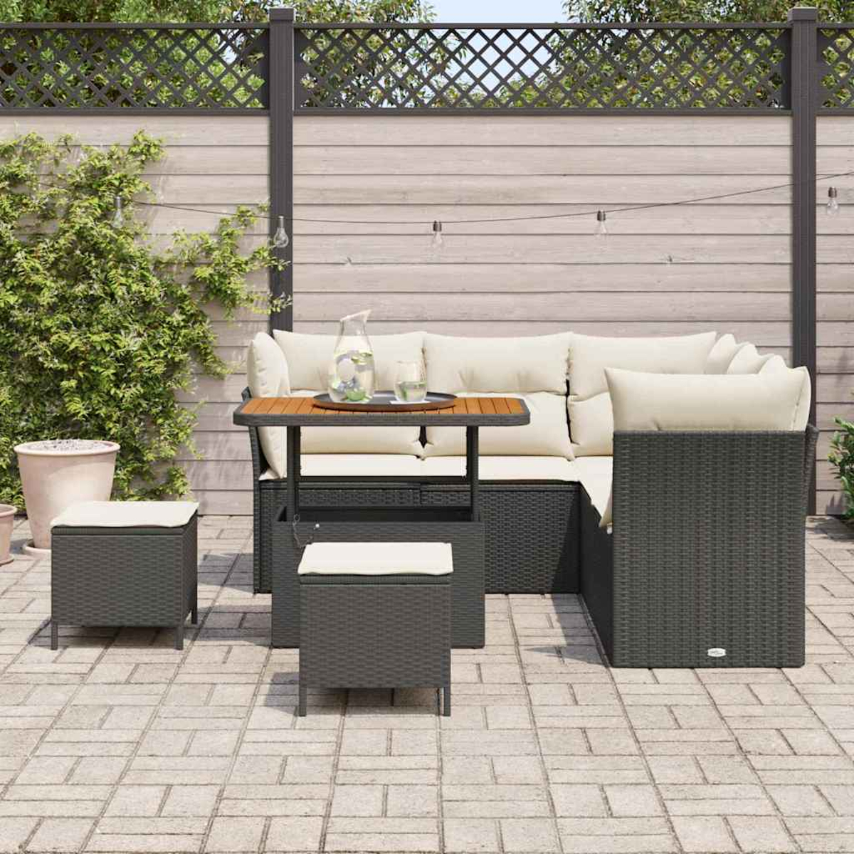 Outdoor-Terrassenset mit grau gewebten Möbeln, cremefarbenen Kissen, kleinem Tisch und zwei Hockern, mit Holzzaun im Hintergrund.