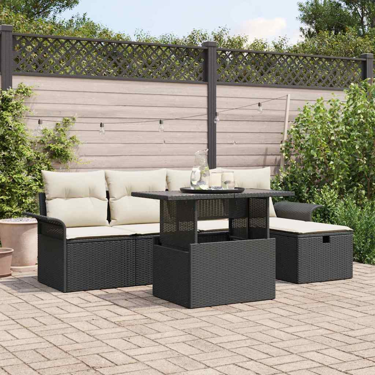 Gartenmöbel-Set: schwarzes Korbmöbel-Sofa, Tisch und Chaiselongue mit cremefarbenen Kissen auf einer gepflasterten Terrasse.