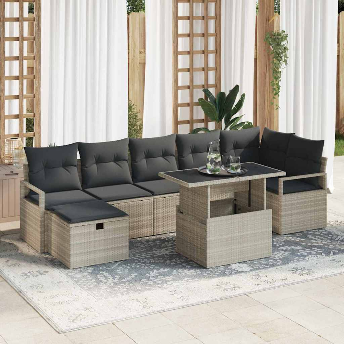 Garten-Terrassenset mit grauen Kissen, einem Tisch mit Getränken und einem Teppich. Weiße Vorhänge und Holzgitter im Hintergrund.