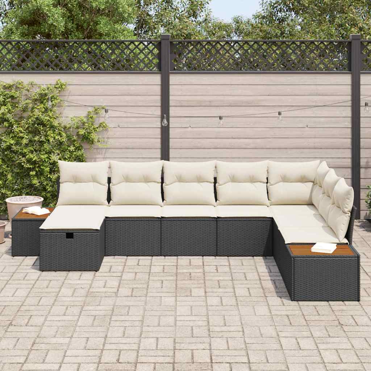 Outdoor-Ecksofa mit beigen Kissen und dunkelgrauem Korbgeweberahmen. Im Hintergrund ein Holzzaun und Grün.