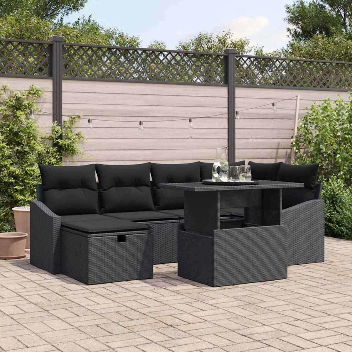 Schwarzes Outdoor-Korbmöbelset auf einer Terrasse. Enthält ein Sofa, einen Hubtisch und eine Aufbewahrungshocker, umgeben von Grün.