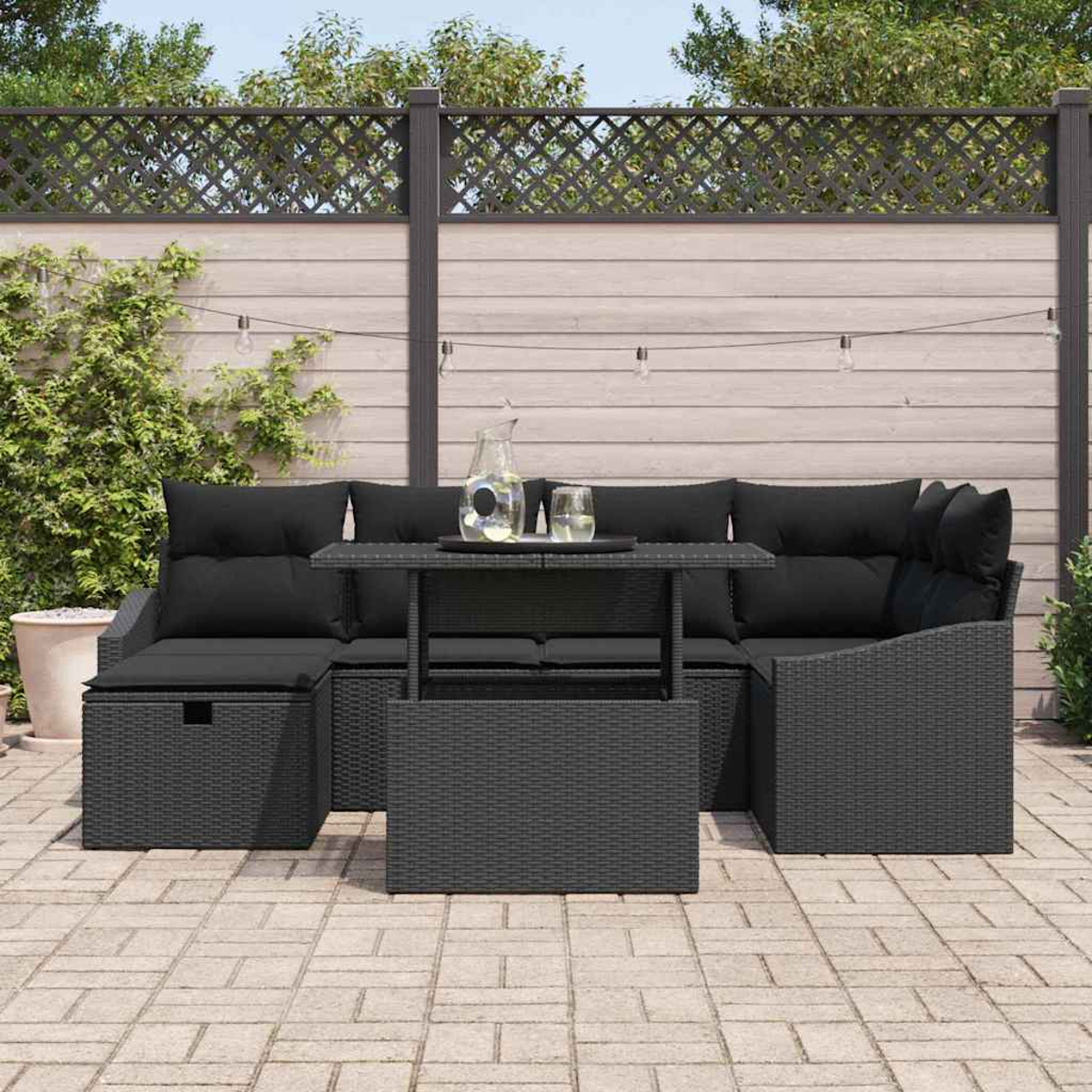 Szene im Freien mit schwarzem Korbmöbel-Set. Beinhaltet einen Tisch, ein Ecksofa und einen dekorativen Zaun im Hintergrund.
